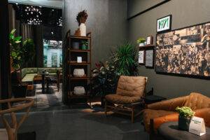 A cozy interior featuring a green corner seating area, wooden shelves with decorative items, and plants. Soft lighting enhances the inviting atmosphere.