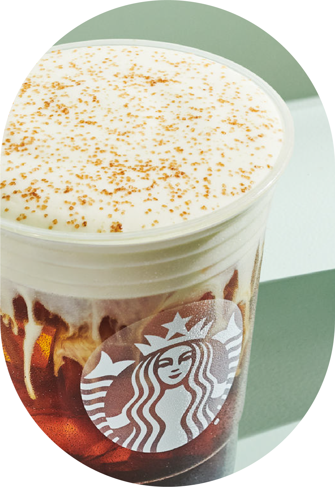 A clear cup filled with iced coffee topped with whipped cream and a sprinkle of cinnamon. The cup features a logo.