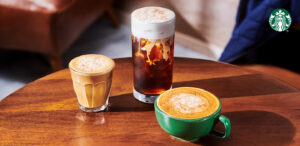 Three coffee drinks are displayed on a wooden table: a small glass of iced coffee, a tall glass with layered cold brew, and a green cup of a creamy beverage, all topped with a sprinkle of cinnamon.