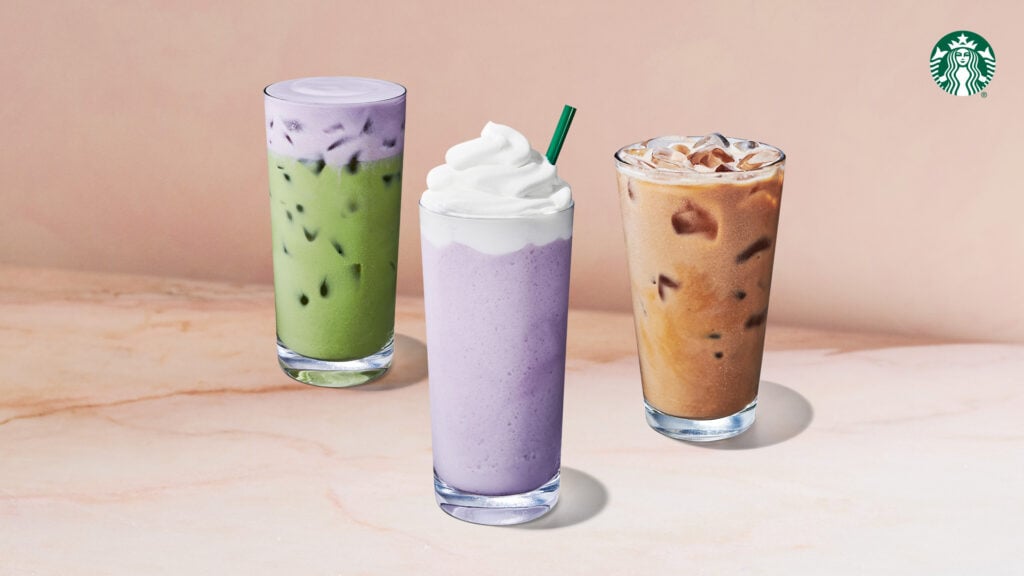 Three colorful beverages are displayed: a green iced drink, a purple whipped drink topped with cream, and a brown iced coffee.