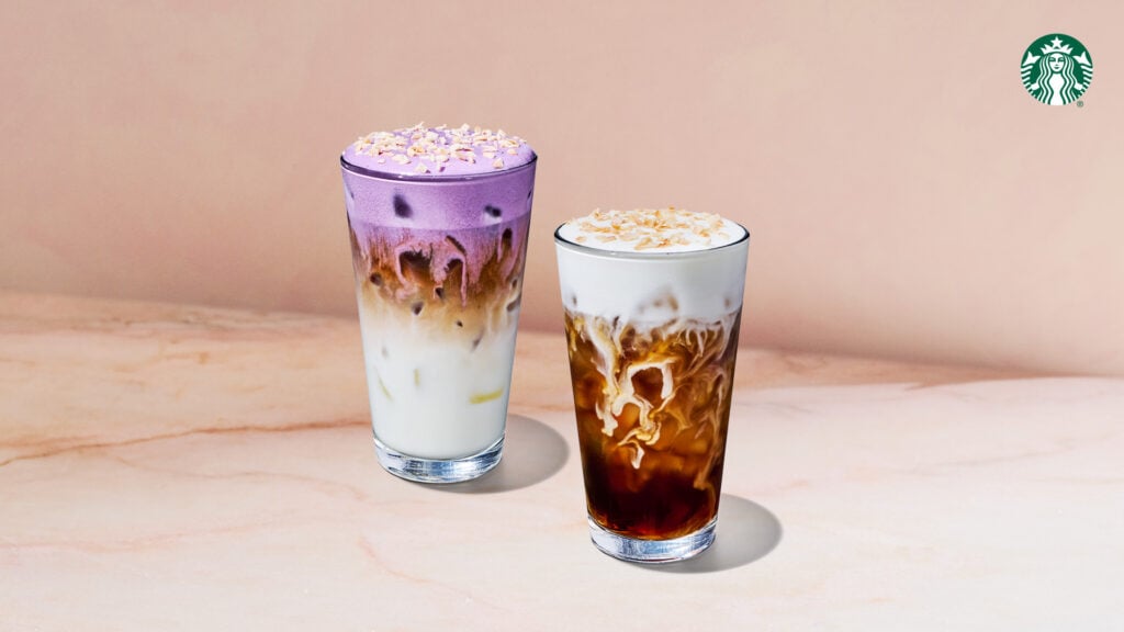 Two iced beverages are displayed: one with a purple layer topped with whipped cream and coconut flakes, and the other a dark iced coffee with a creamy layer and similar toppings. Both are served in clear glasses against a soft, neutral background.