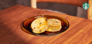 Two round, golden-brown baked goods are placed on a dark amber plate, resting on a wooden table.