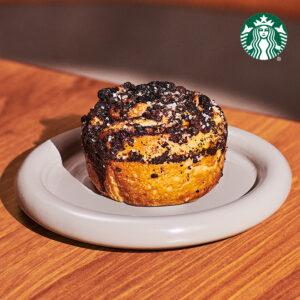 A cinnamon roll with a crumbly topping sits on a light gray plate, placed on a wooden surface.