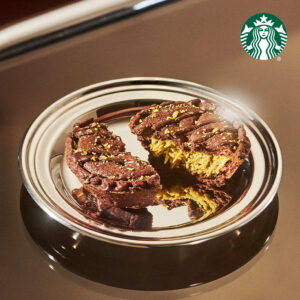 A chocolate cookie is split in half, revealing a creamy filling, topped with green sprinkles, on a reflective silver plate.