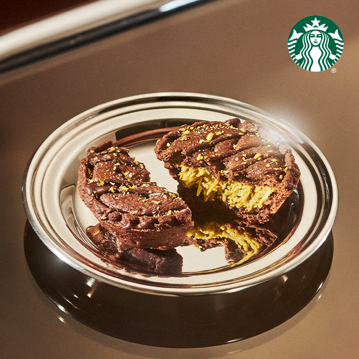 A chocolate cookie is split in half, revealing a creamy filling, topped with green sprinkles, on a reflective silver plate.