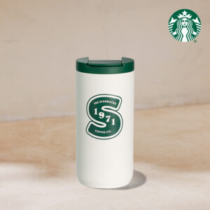 A white travel mug with a green lid features a circular logo that reads "THE STARBUCKS 1971 COFFEE CO." on the front.