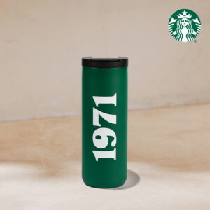 A green travel mug with a black lid features the number "1971" in white. The background is a neutral, light-colored surface.
