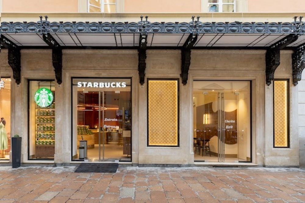 A storefront featuring a Starbucks with a prominent logo and glass doors. Adjacent is another entrance with decorative elements.