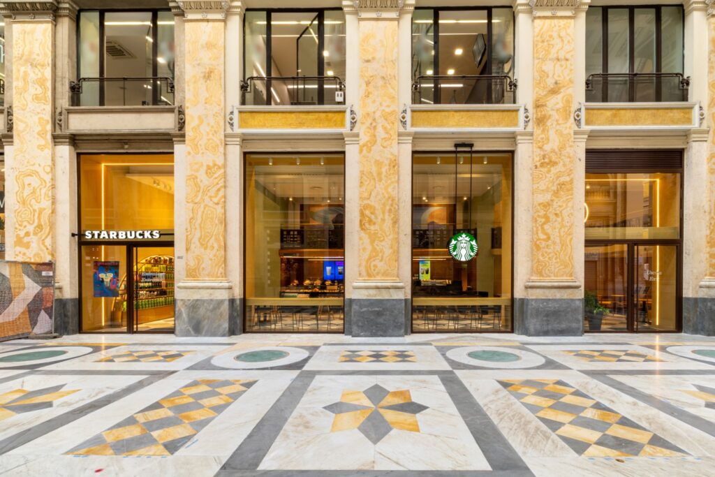 A stylish café with large glass windows, featuring a Starbucks sign. The floor has intricate geometric patterns in marble.