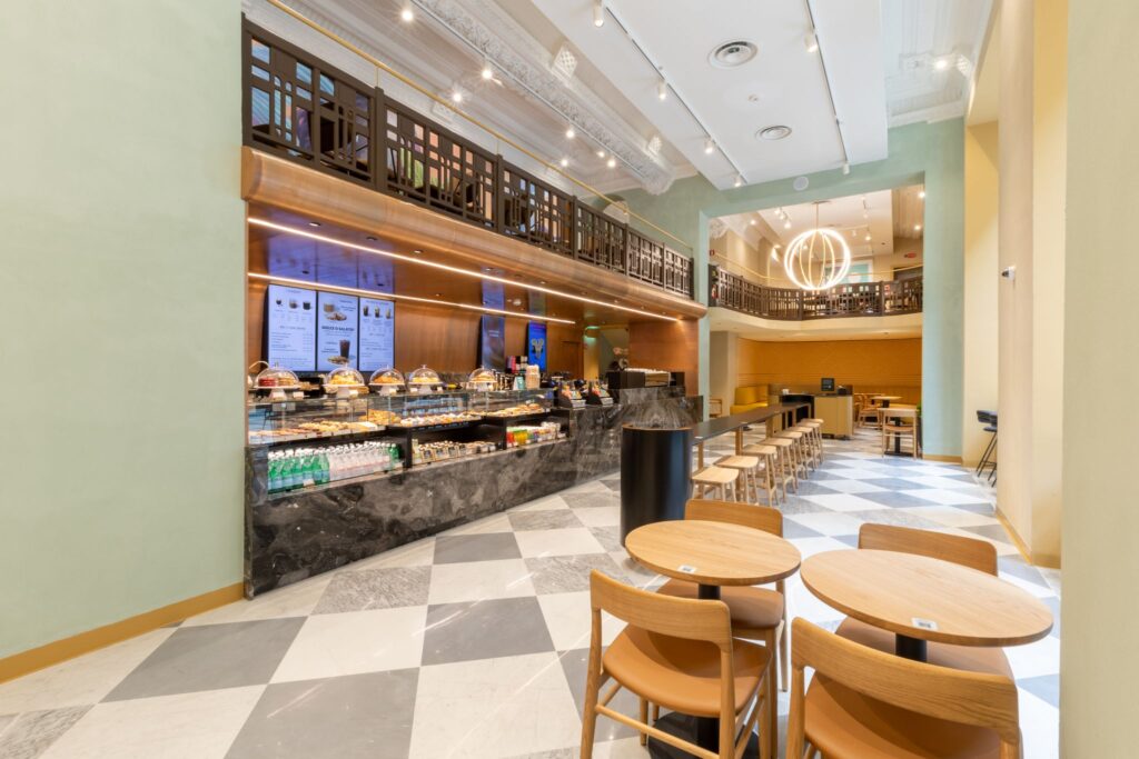 A modern café interior featuring a sleek counter with various pastries and drinks, surrounded by wooden seating and stylish decor.