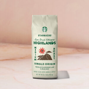 A bag of Starbucks Sun-Dried Ethiopia Highlands coffee, featuring a design with a mountain, sun, and text indicating it's a medium roast, single-origin coffee with notes of blackberry jam and wild mint. The bag is 16 oz (453 g) and highlights that it contains whole bean 100% Arabica coffee.