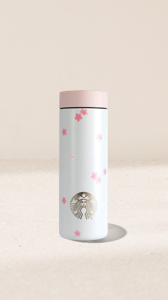 A white stainless steel tumbler with a pink lid, decorated with pink cherry blossom designs and a gold Starbucks logo.