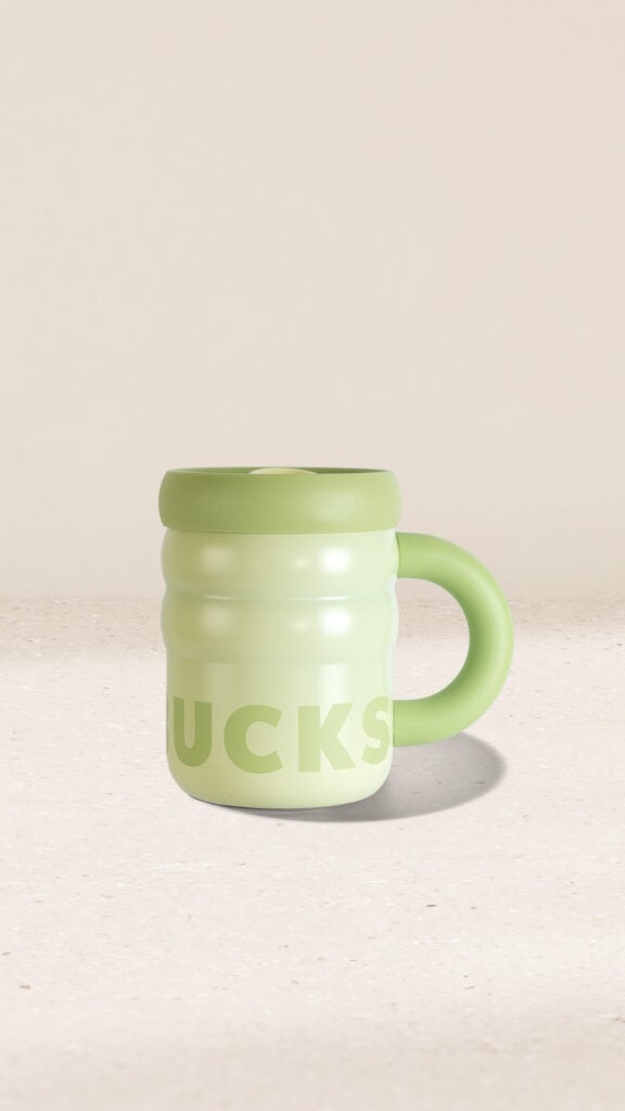 A light green mug with a rounded shape and a thick handle, featuring the word "BUCKS" in bold lettering. The background is neutral.