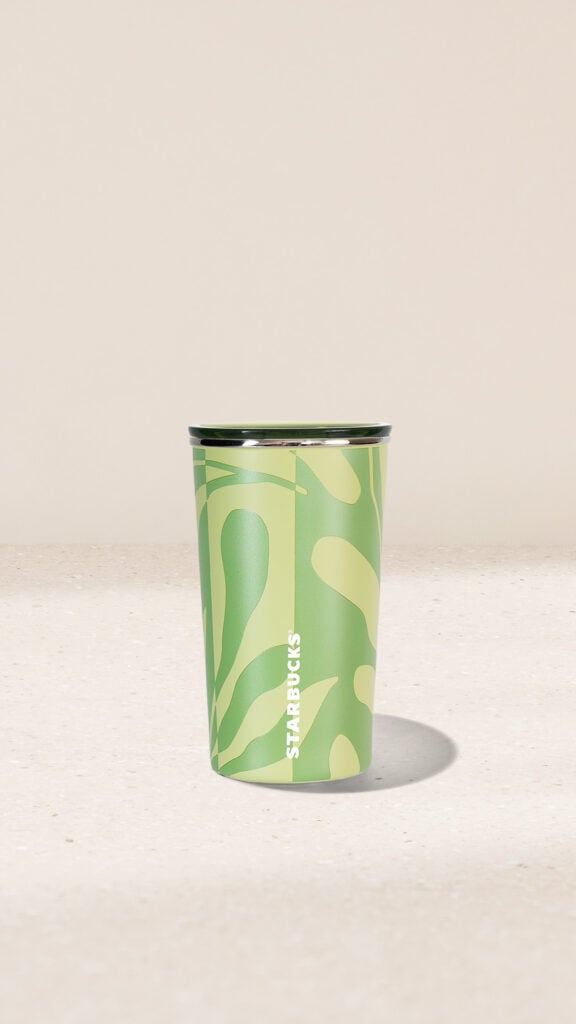 A green Starbucks cup with a wavy pattern and a silver rim, placed on a light-colored surface.