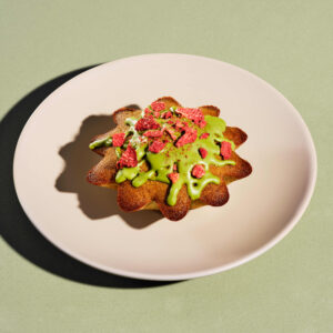 A star-shaped pastry topped with green icing and crushed red strawberries, placed on a pale plate against a green background.