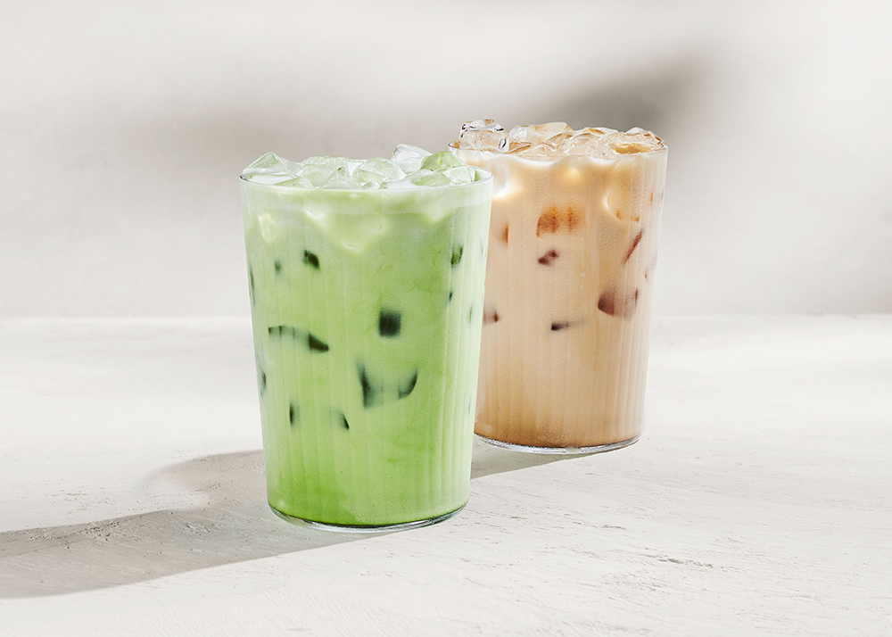 Two tall glasses filled with ice-cold beverages sit side by side. The left glass contains a light green drink, while the right glass holds a creamy brown drink with ice cubes. The background is neutral and minimalistic.