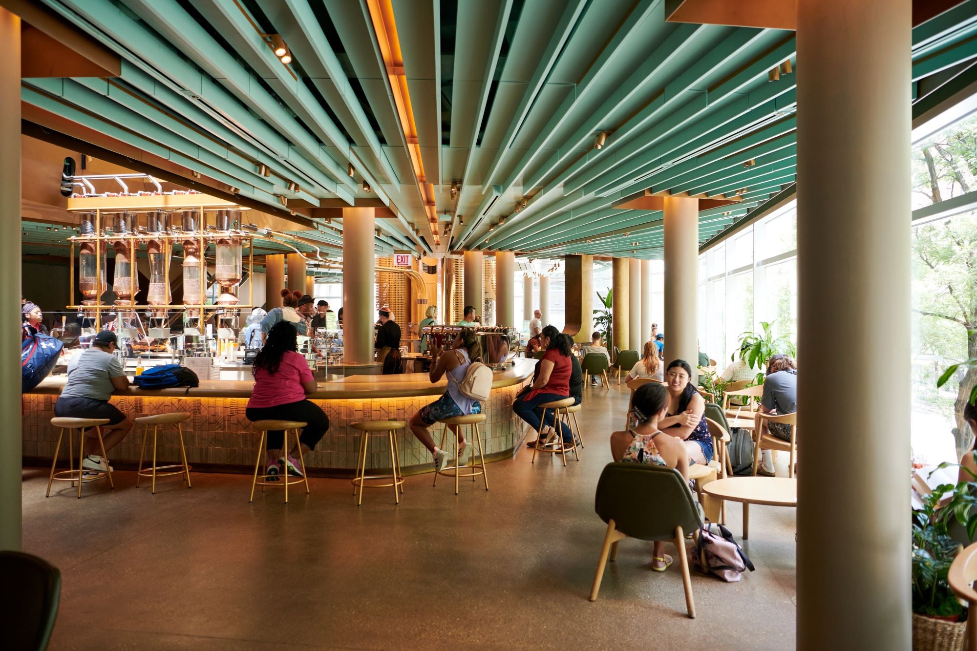 A modern café interior featuring a curved bar with seating, vibrant teal ceiling beams, and large windows allowing natural light.