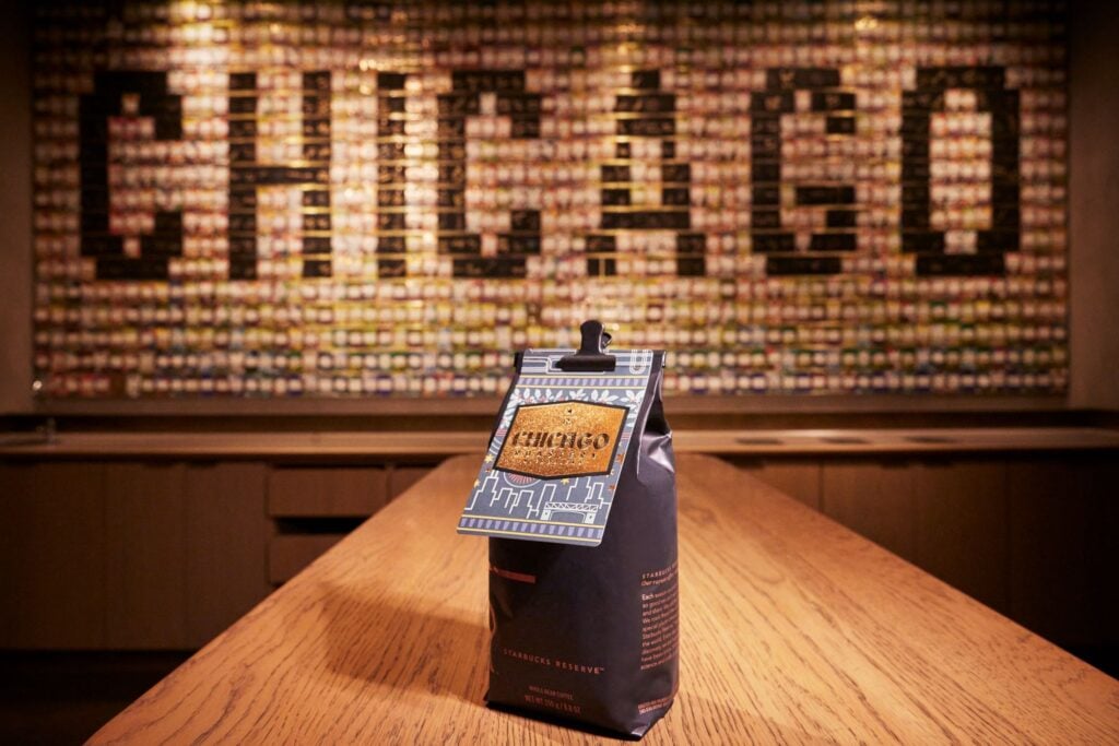 A coffee bag labeled "Chicago" is prominently displayed on a wooden table, with a colorful wall of small items behind it spelling "CHICAGO.