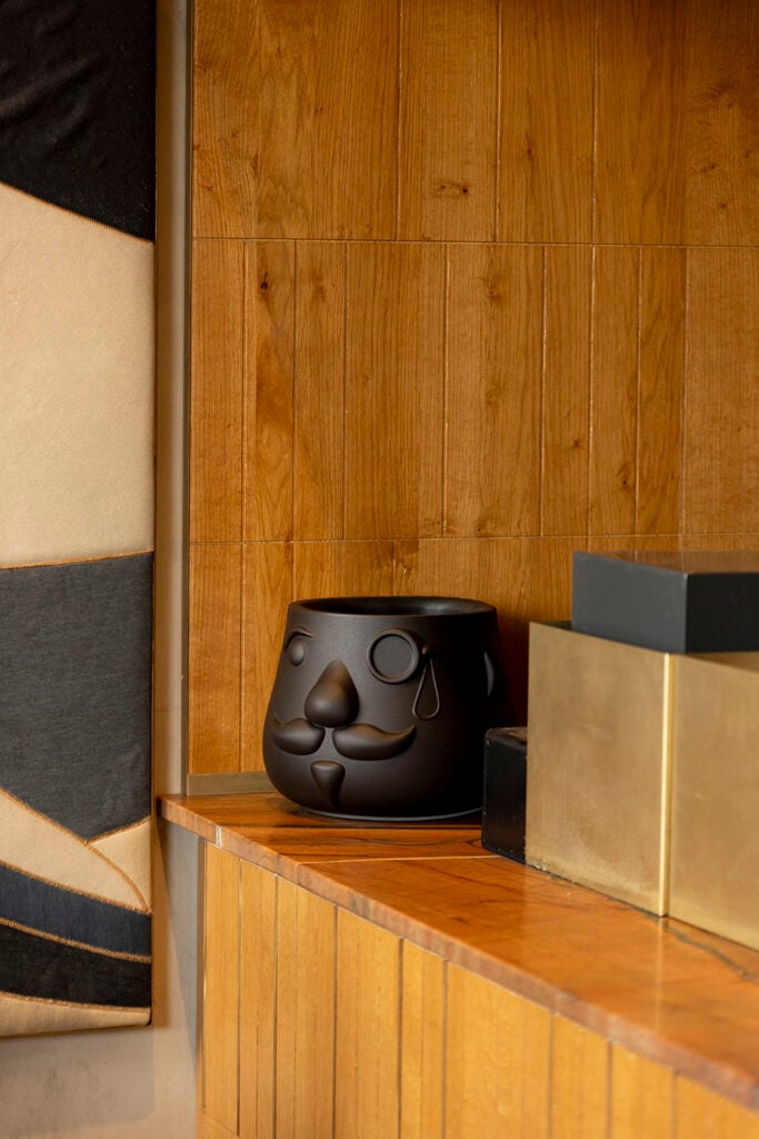 A black decorative planter with a smiling face and a teardrop sits on a wooden shelf, alongside geometric black and gold boxes.