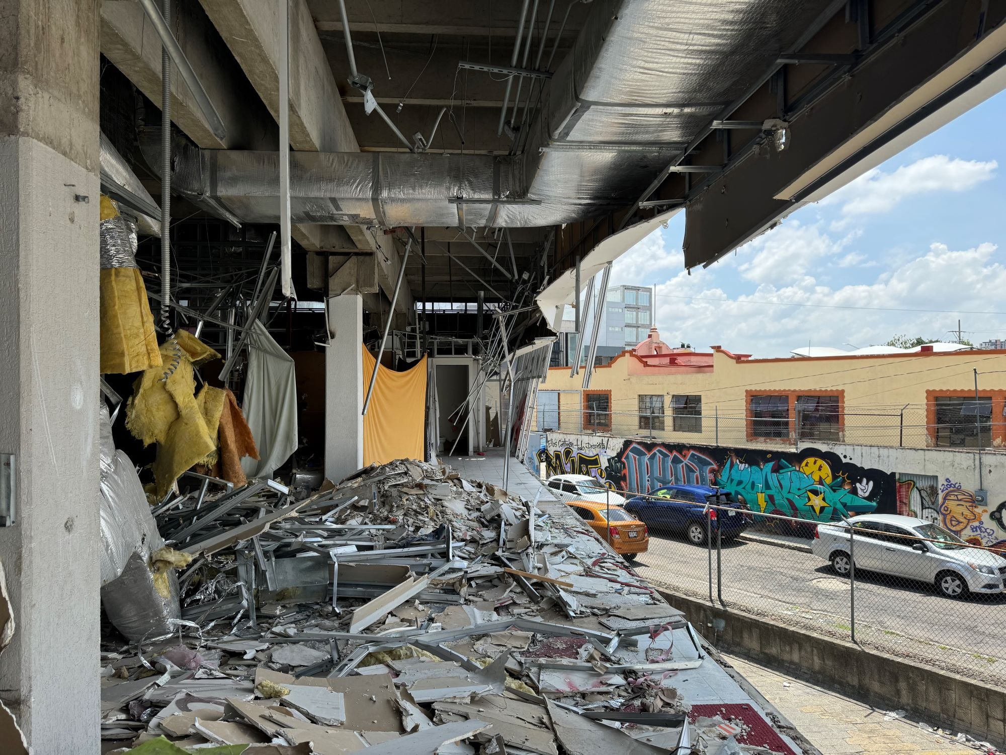 A partially demolished interior shows debris, exposed structures, and hanging materials. Outside, colorful graffiti decorates nearby buildings.