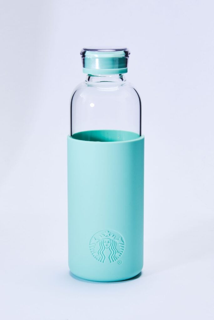 A clear glass water bottle with a mint green silicone sleeve and cap, featuring a raised logo at the base.