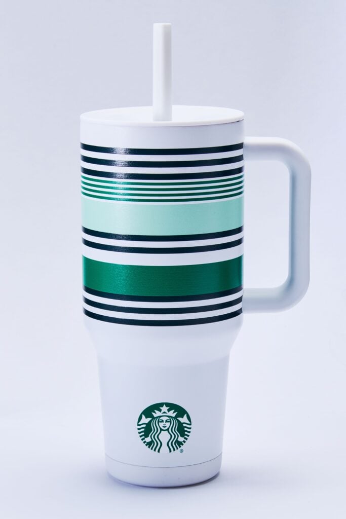 A tall, white Starbucks tumbler features a striped design in shades of green and black, with a white straw and handle.