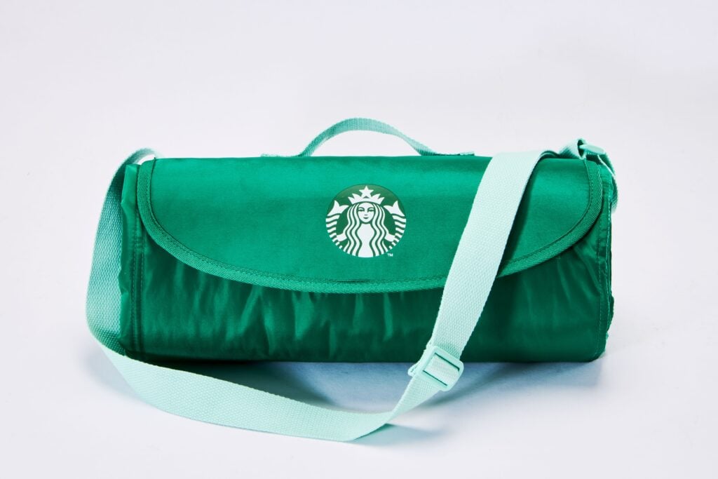 A green bag with a flap and a shoulder strap, featuring the Starbucks logo prominently on the front.