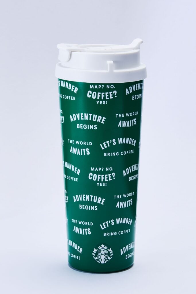 A green travel mug features various white phrases like "ADVENTURE BEGINS" and "LET'S WANDER," along with the Starbucks logo.