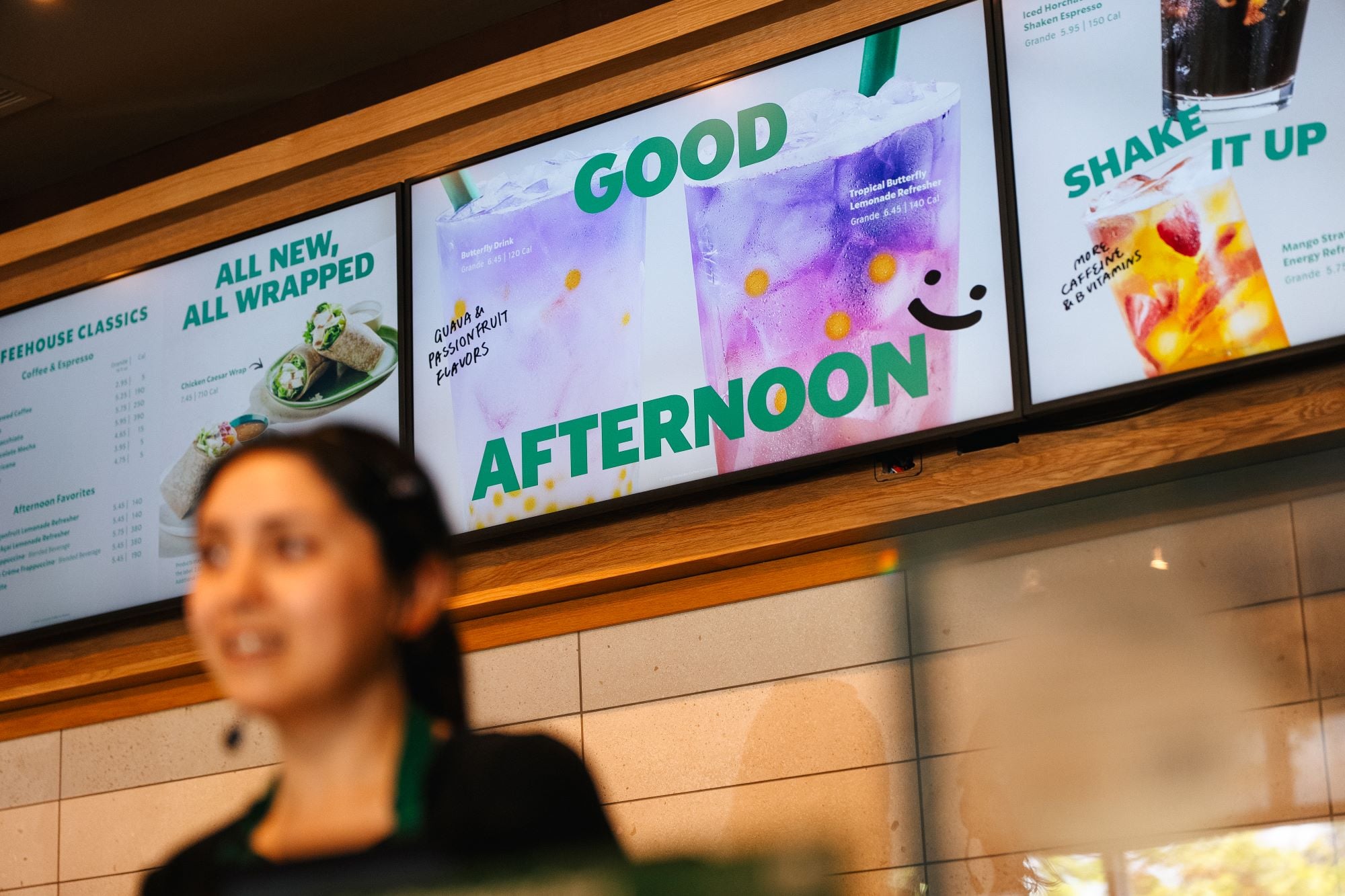 A menu board displays colorful drinks, including a Butterfly Refresher and a Tropical Lemonade, with a cheerful greeting.