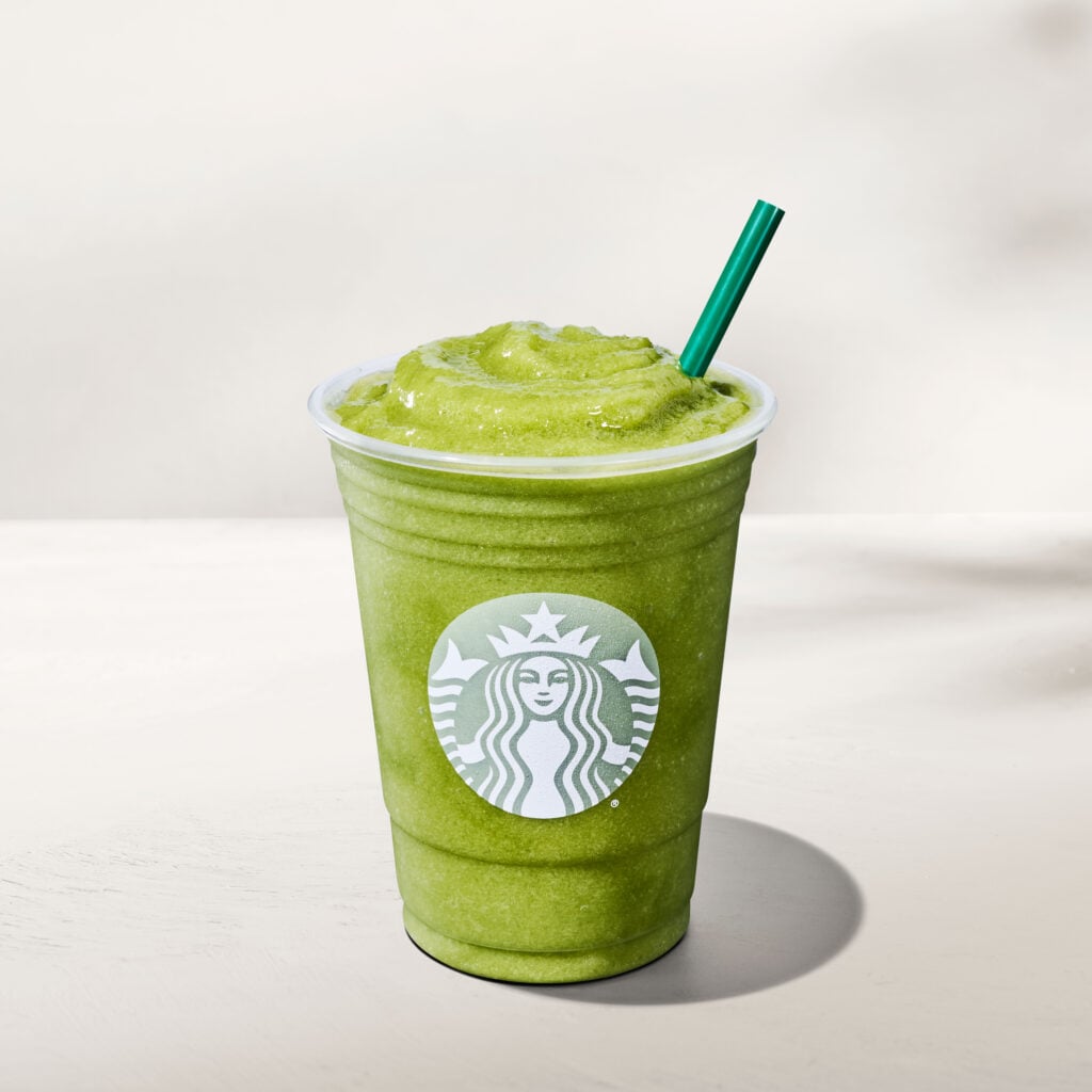 A green frozen beverage in a clear cup with a green straw, featuring the Starbucks logo prominently on the front.