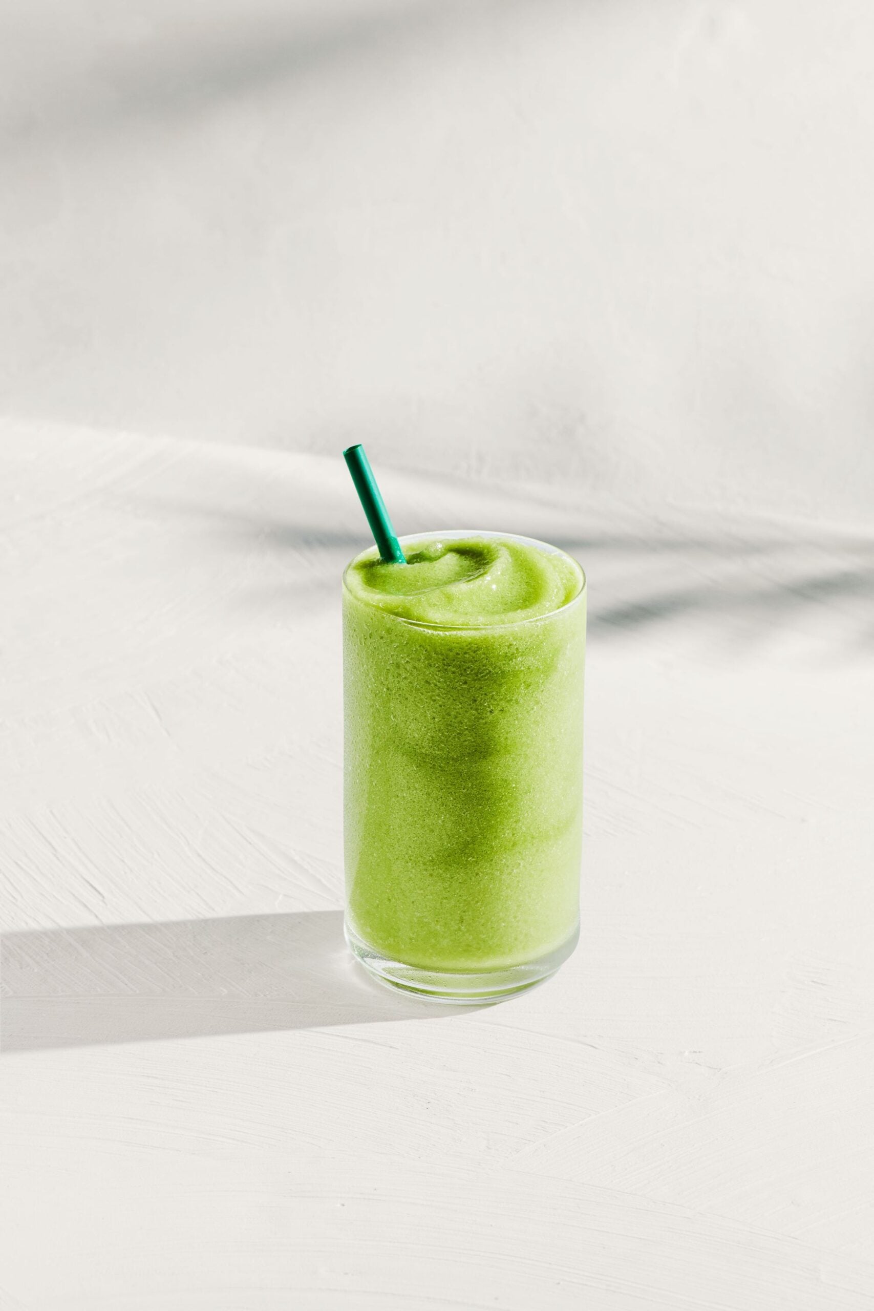 A tall glass filled with a smooth, vibrant green beverage, topped with a green straw, sits on a light-colored surface.