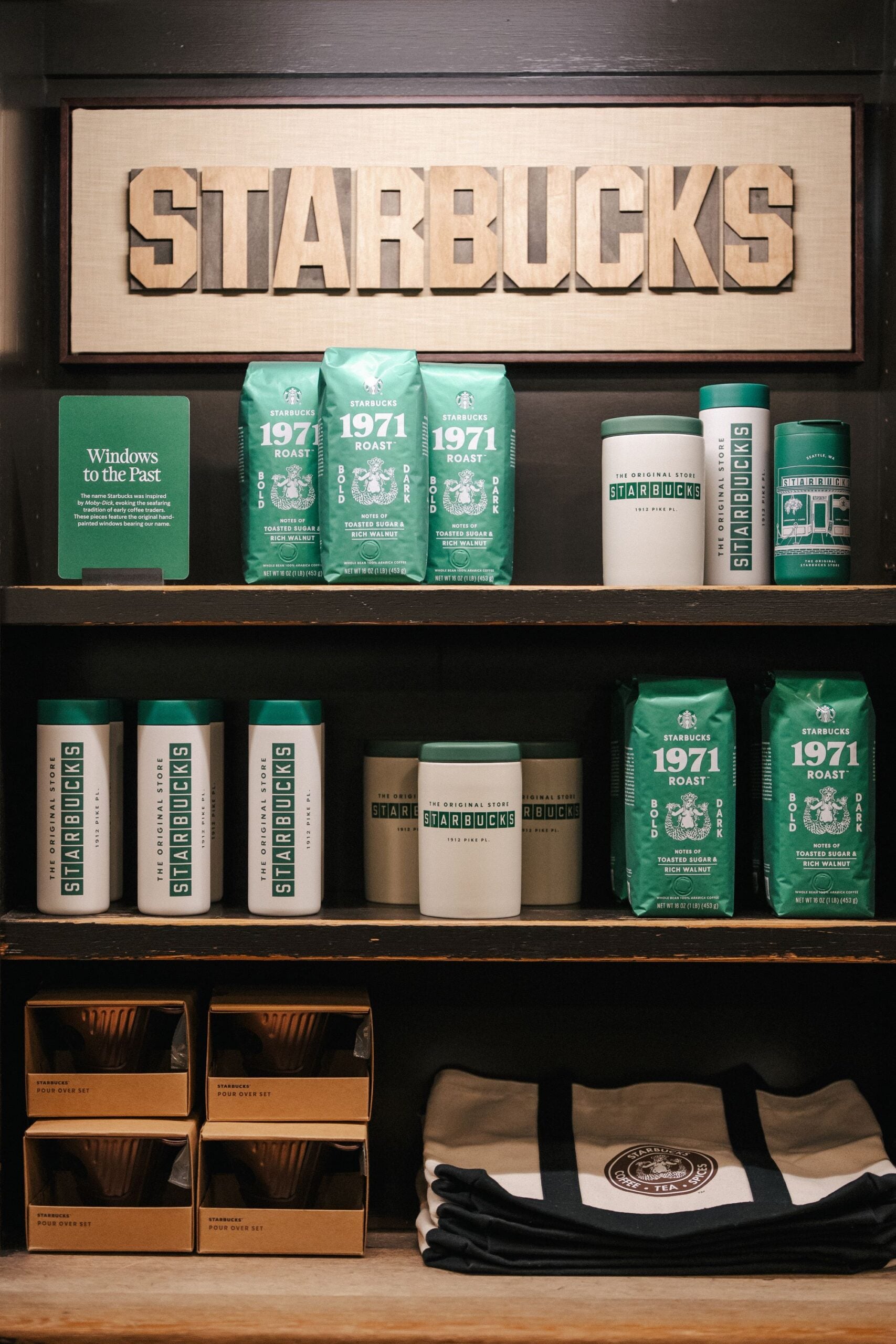 Shelves display various Starbucks merchandise, including bags of 1971 Roast coffee, mugs, and a pour-over set, with a sign reading "Windows to the Past.