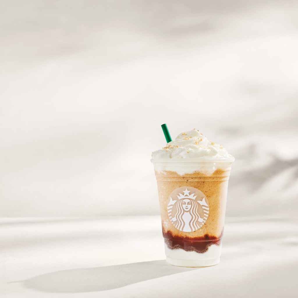 A Starbucks beverage in a clear cup features layers of blended coffee, topped with whipped cream and a green straw.