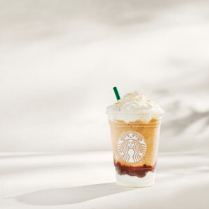 A Starbucks beverage in a clear cup features layers of blended coffee, topped with whipped cream and a green straw.