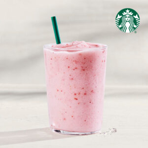 A frosty pink smoothie in a clear glass with a green straw, featuring a creamy texture and small fruit pieces.
