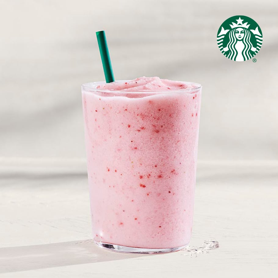 A frosty pink smoothie in a clear glass with a green straw, featuring a creamy texture and small fruit pieces.