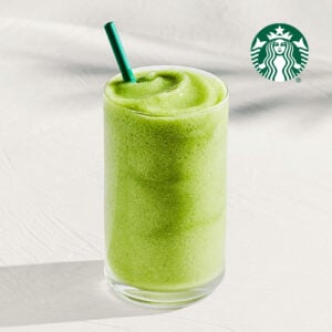 A tall glass filled with a smooth, vibrant green beverage, topped with a green straw, sits on a light surface.