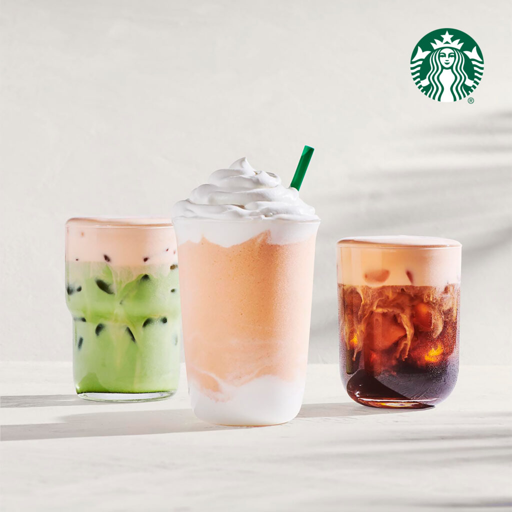 Three beverages are displayed: a green iced drink layered with pink, a creamy orange frappuccino topped with whipped cream, and a dark iced coffee.