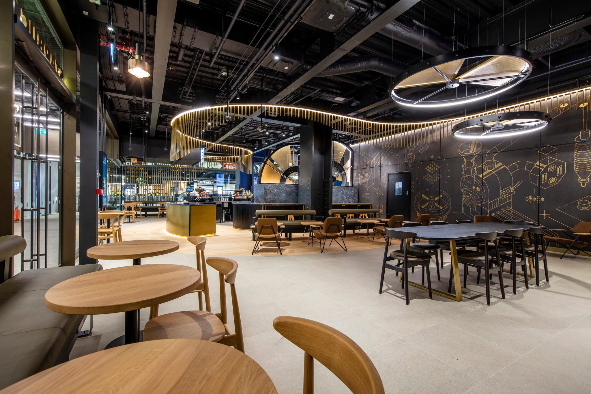 A modern café interior featuring wooden tables and chairs, a sleek bar area with a gold accent, and stylish lighting fixtures.