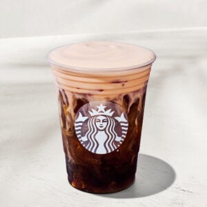 A clear cup filled with iced coffee, featuring a creamy, light-colored foam on top. The cup has a Starbucks logo.