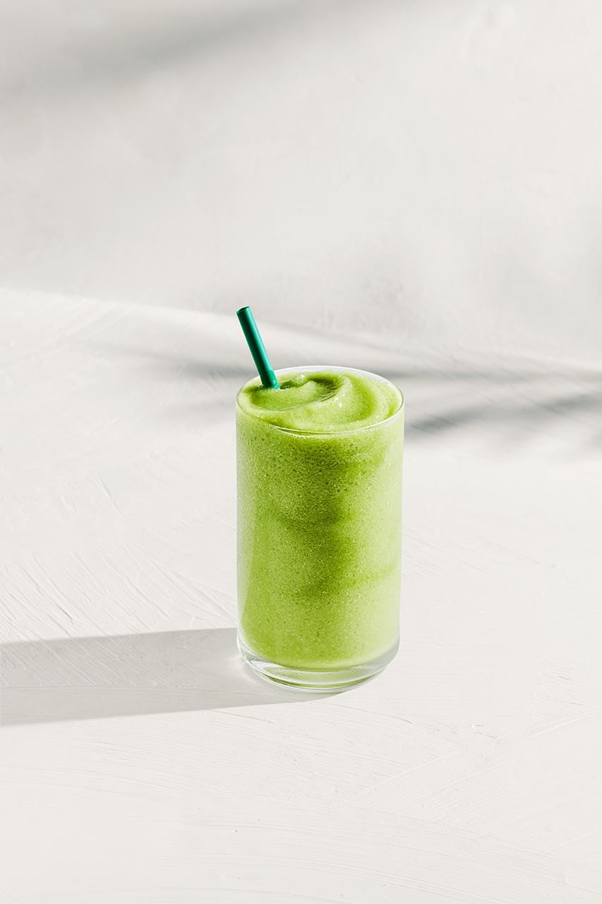 A tall glass filled with a smooth, vibrant green beverage, topped with a green straw, sits on a light textured surface.