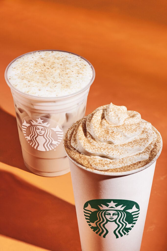 Two coffee drinks are displayed against an orange background. On the left, an iced drink in a clear cup topped with foam and sugar. On the right, a hot drink in a paper cup with whipped cream and a dusting of cinnamon. Both feature the Starbucks logo.