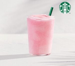 A tall glass filled with a frosty, pink beverage topped with a green straw, set against a light background.