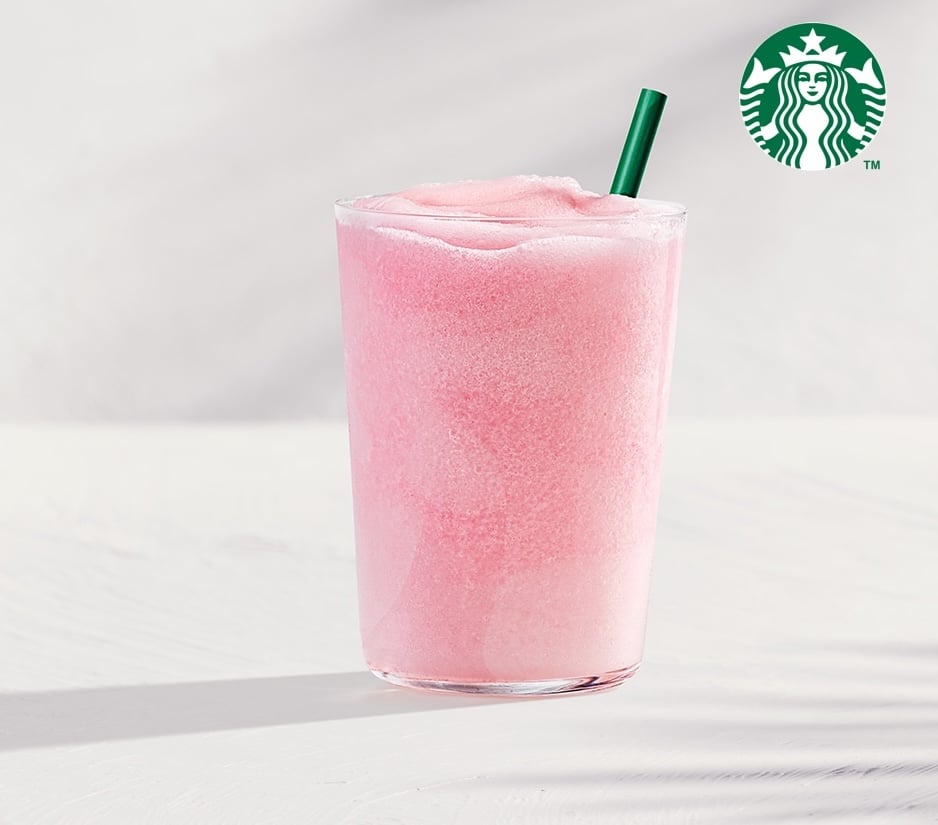 A tall glass filled with a frosty, pink beverage topped with a green straw, set against a light background.