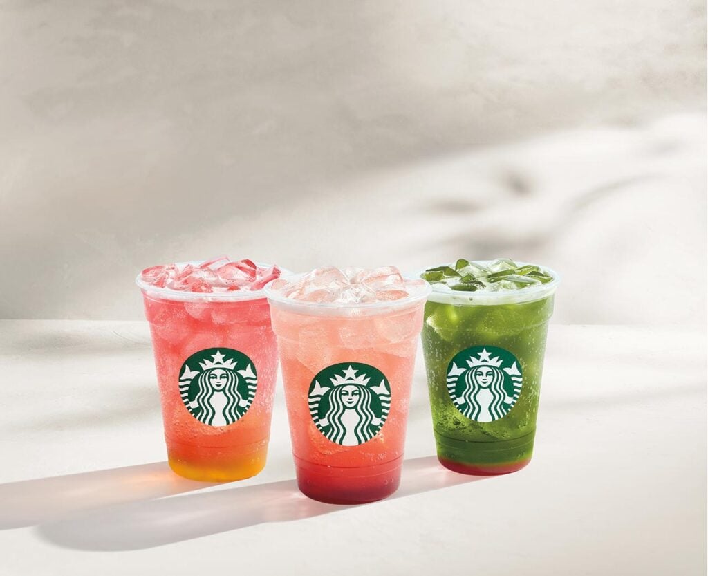Three iced beverages in clear cups with the Starbucks logo. The drinks are vibrant pink, red, and green, filled with ice.