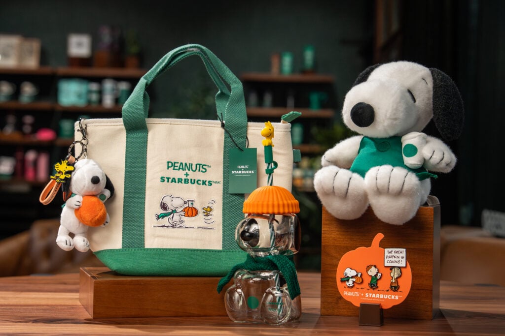Starbucks and Peanuts merch including a tote bag, pins, a Snoopy plush, a clear Snoopy cup.
