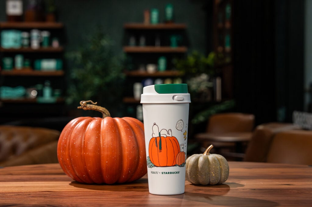A white coffee tumbler with Snoopy laying on a Pumpkin